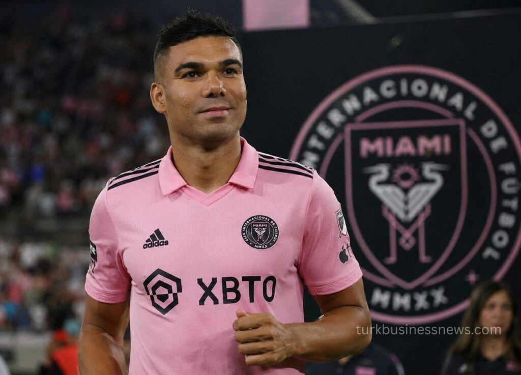 Soccer player in pink kit runs on the field with a crowd in the background and sponsor XBTO on the jersey.