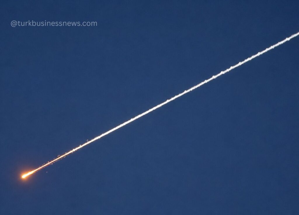 Rocket launch leaving an orange flame and white contrail diagonally across a blue sky.